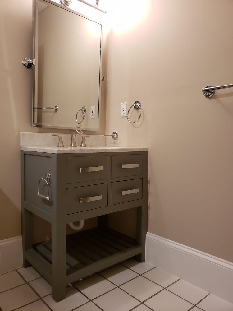 Gray vanity with drawers, a marble countertop, mirror, and towel rack in a bathroom with beige walls and tile floor.