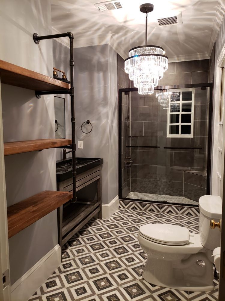 Modern bathroom with gray walls, patterned floor, shower, toilet, shelving, and chandelier.