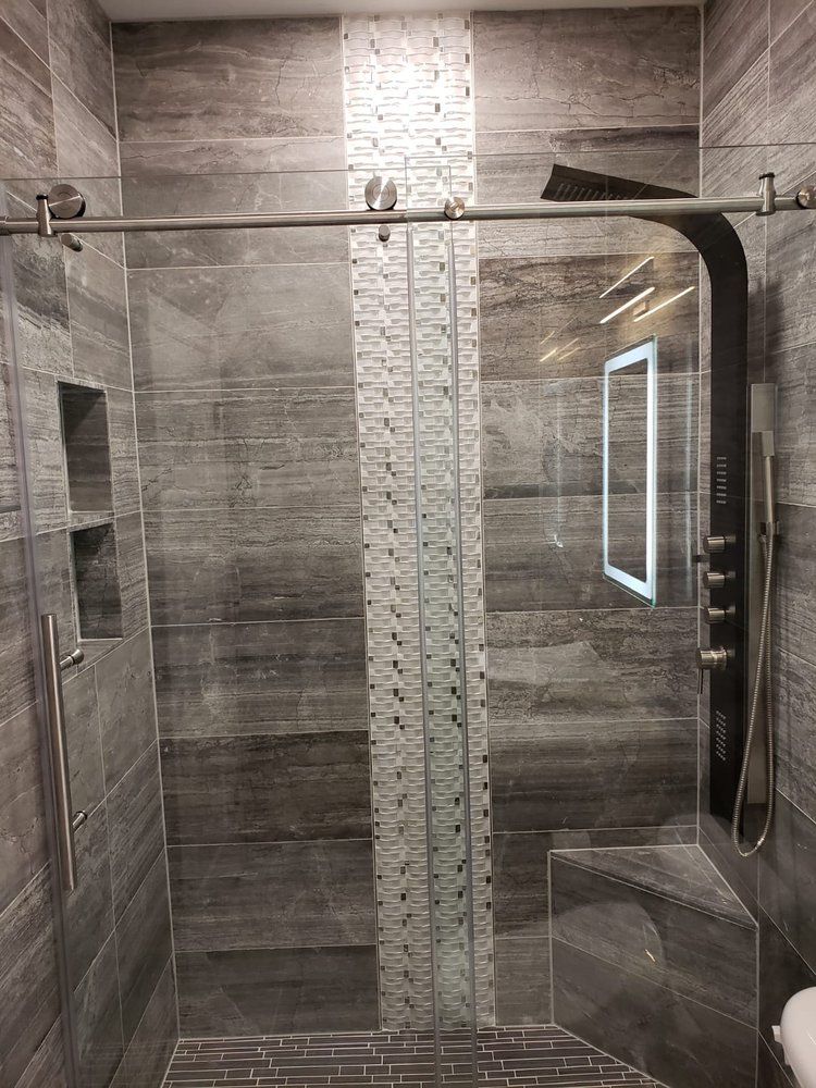 Modern gray tiled shower with glass door and black shower panel.