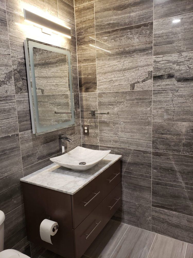 Bathroom with dark brown vanity, vessel sink, marble countertop, and gray tiled walls.