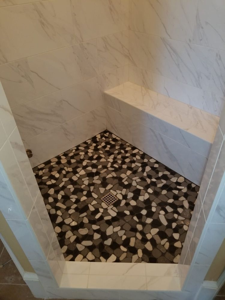 Shower with white marble walls, built-in bench, and pebble stone floor in shades of black, gray, and white.