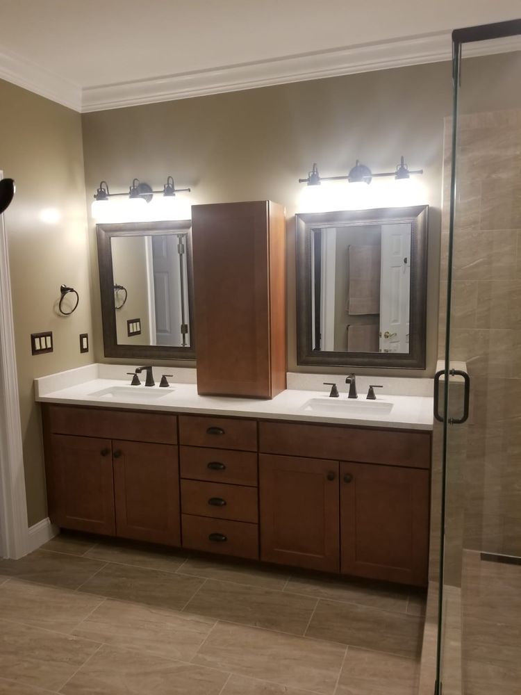Bathroom with double vanity, framed mirrors, and a tall cabinet. Brown cabinets, white countertop.