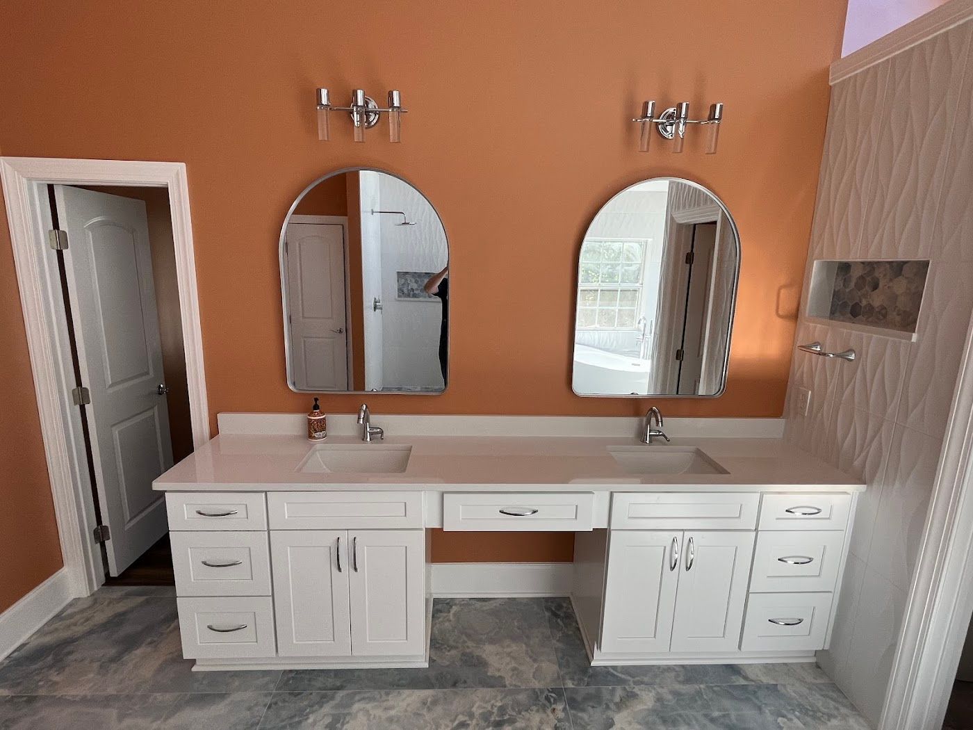 White double vanity with arched mirrors, orange walls, and open door.