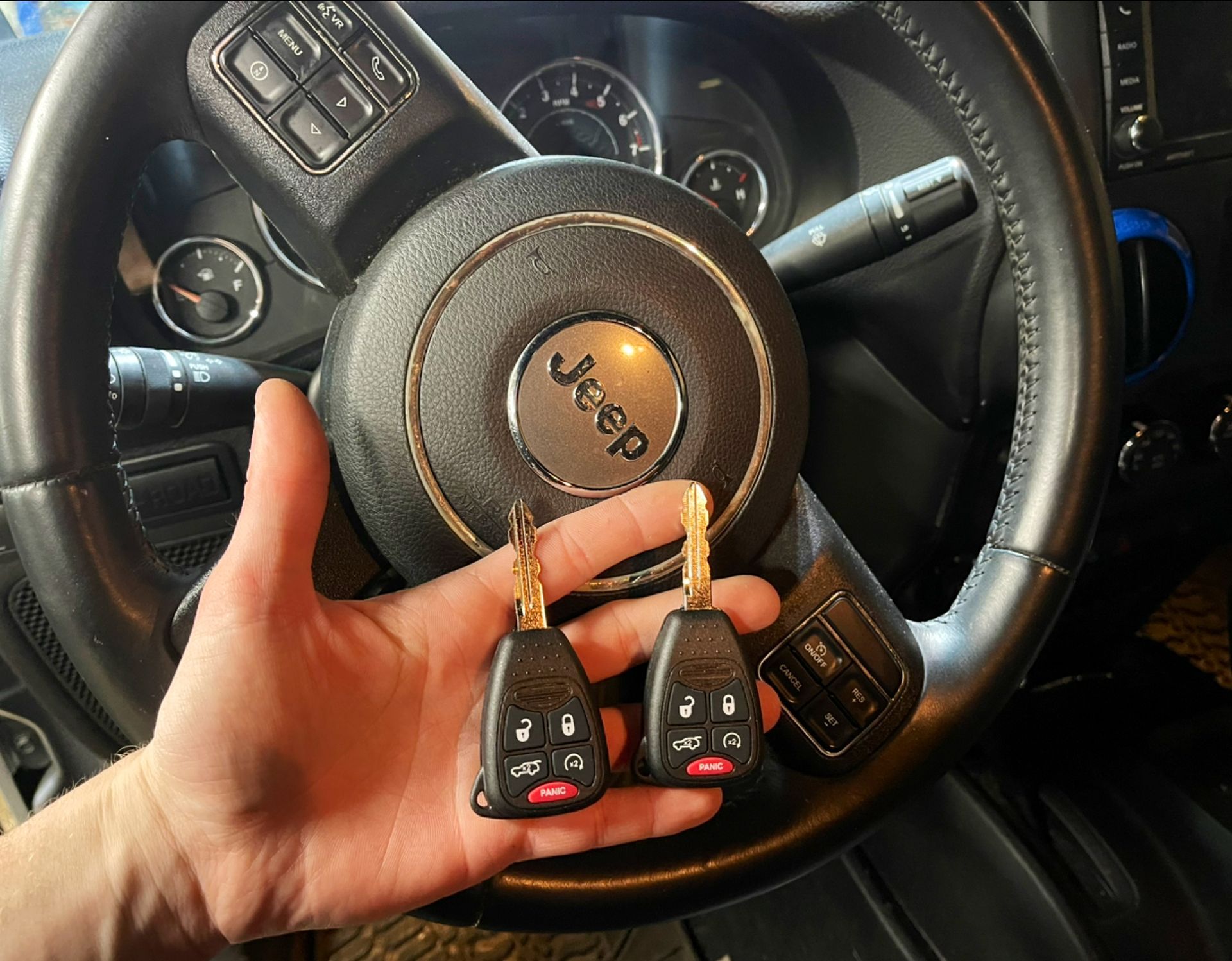 a hand holding a Jeep key in front of a steering wheel