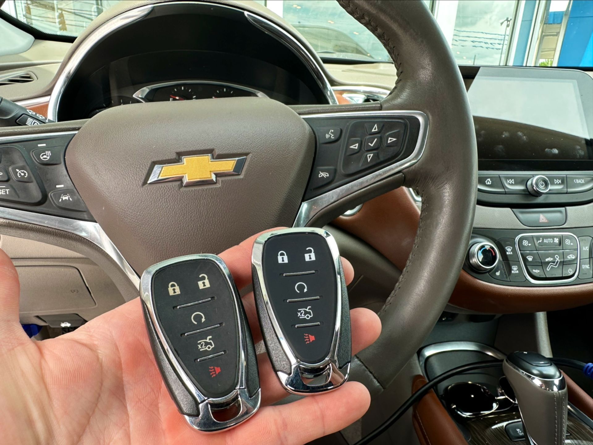 a hand holding two Chevrolet car keys in front of a steering wheel