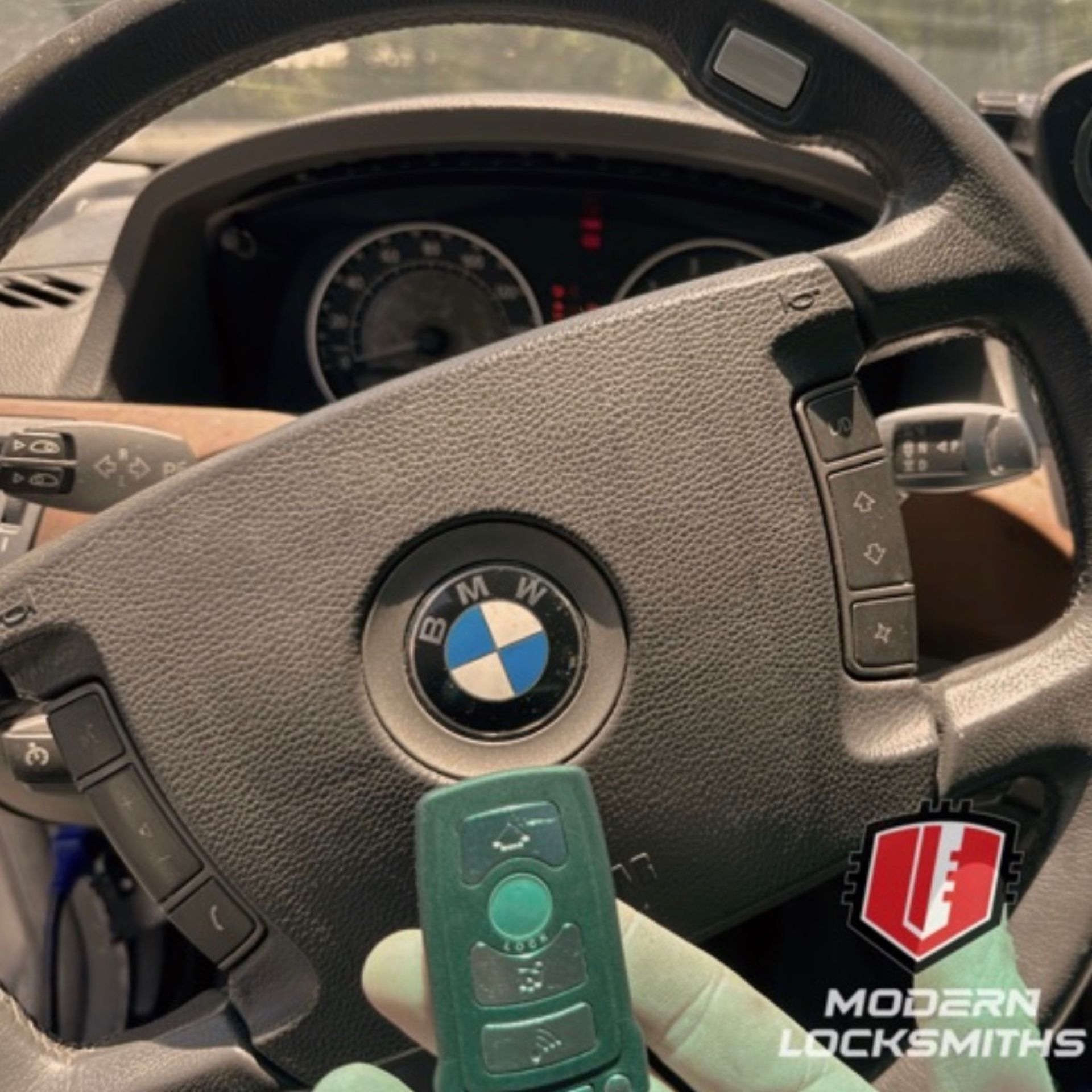 a hand holding a BMW fob  in front of a steering wheel