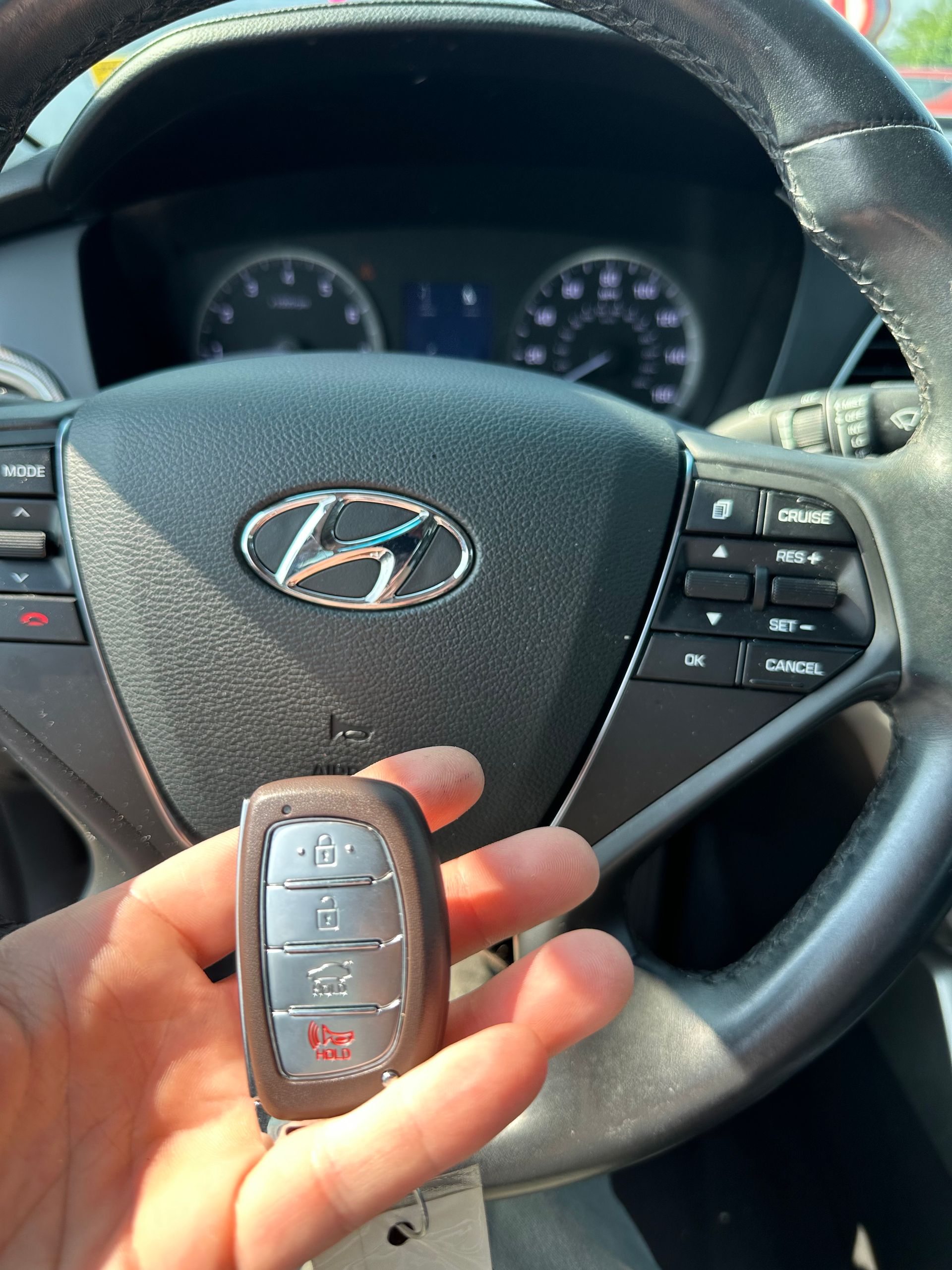 a hand holding a Hyundai vehicle remote in front of a steering wheel
