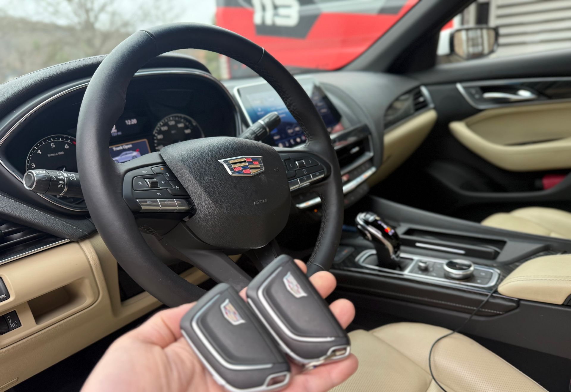 A person is holding a pair of car keys in front of the steering wheel of a car.