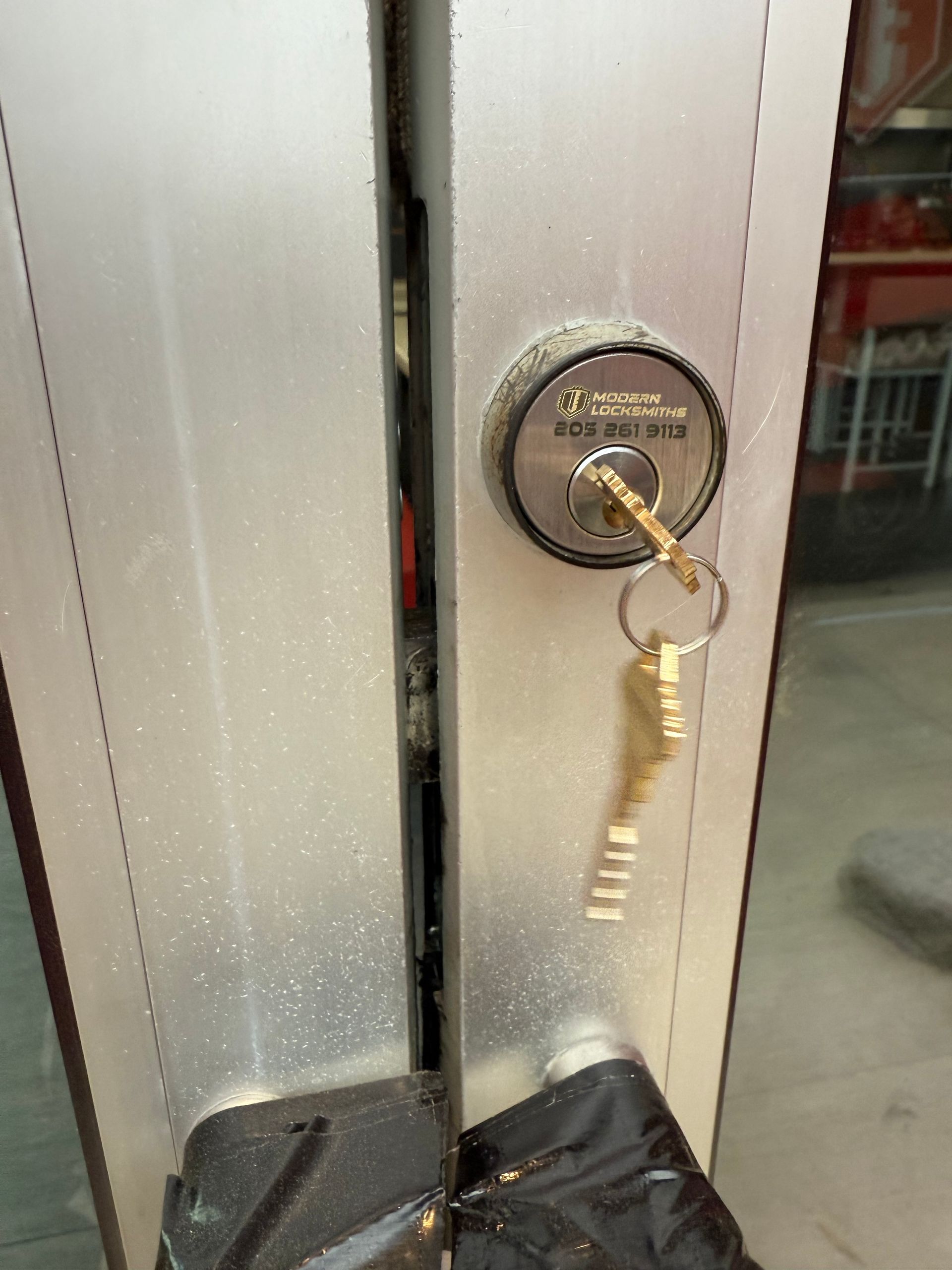 Close-up of a door lock with a key inserted. The door is silver and dirty.