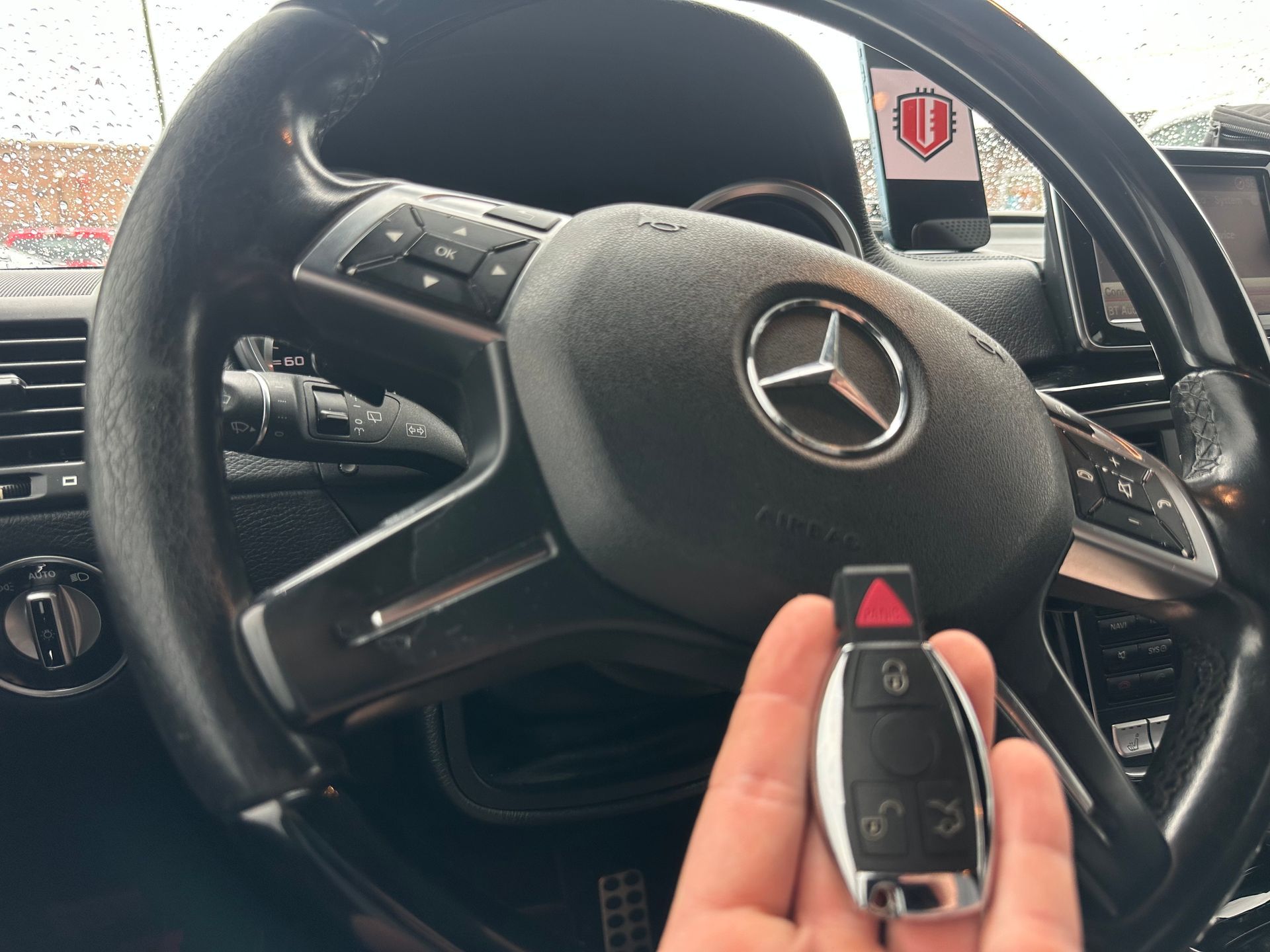 a hand holding a Mercedes key in front of a steering wheel