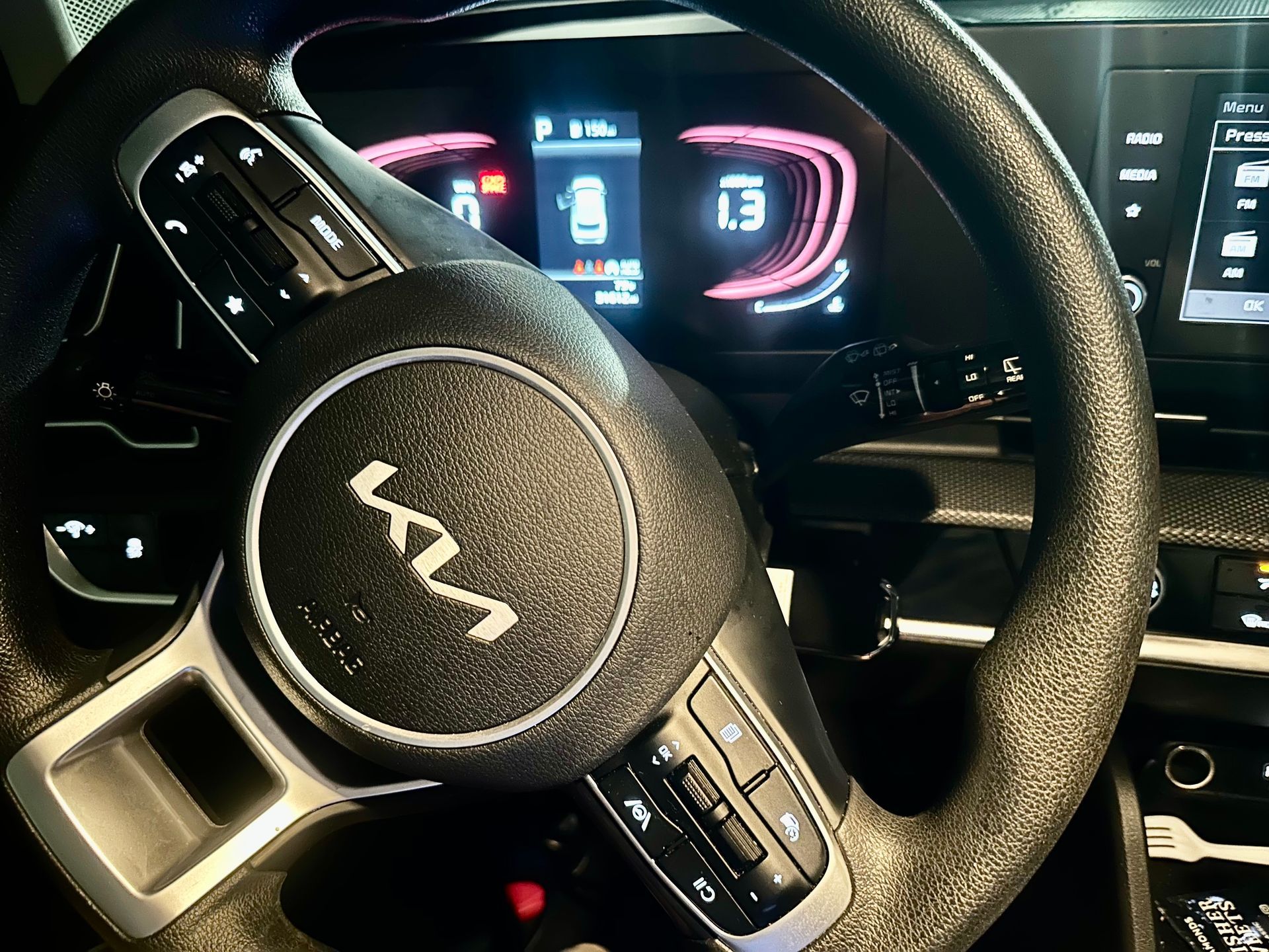 a hand holding a Kia vehicle remote in front of a steering wheel