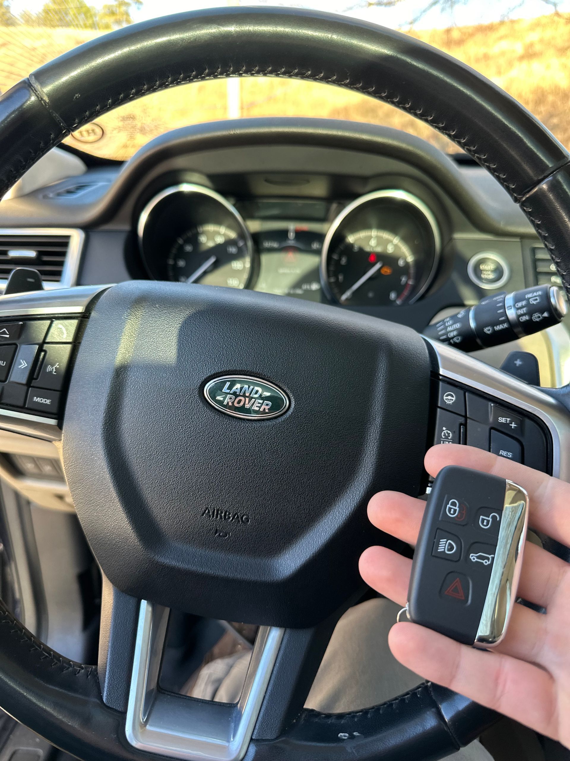 a hand holding a Land Rover vehicle remote in front of a steering wheel