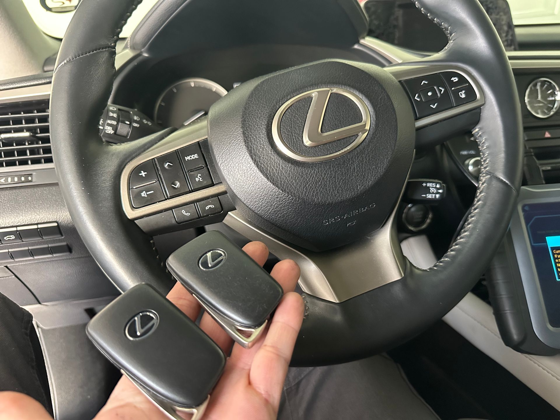 a hand holding a vehicle remote in front of a steering wheel
