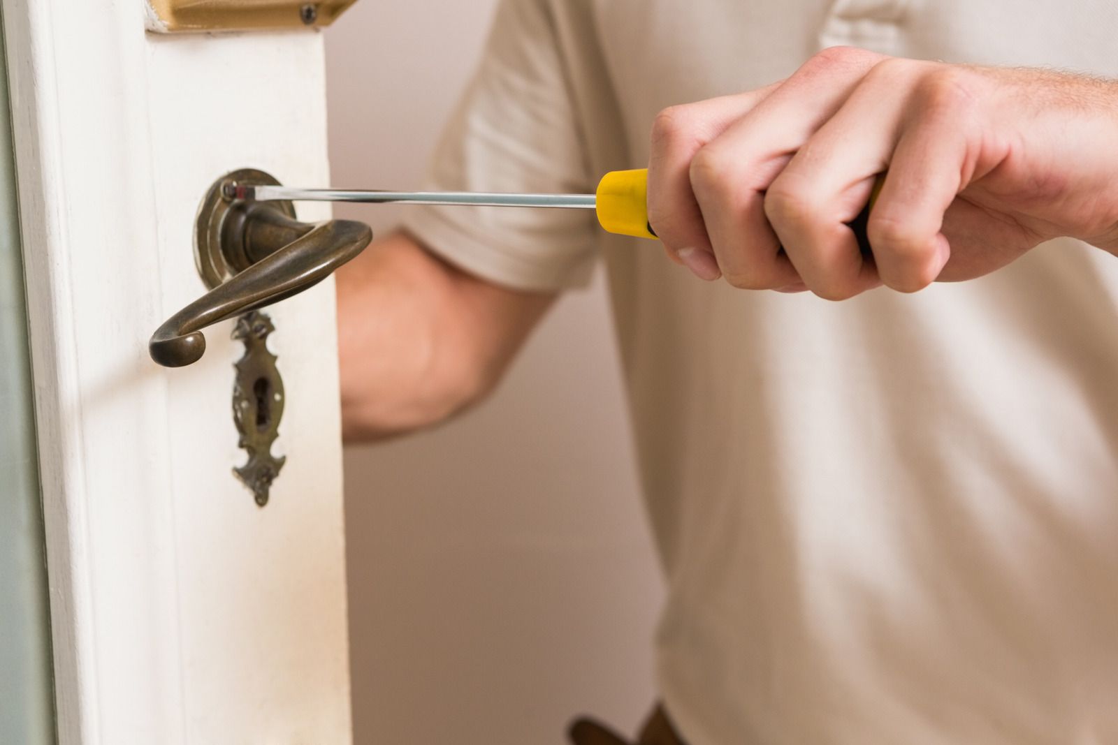 Person using a screwdriver to repair a bronze-colored door handle on a white door.