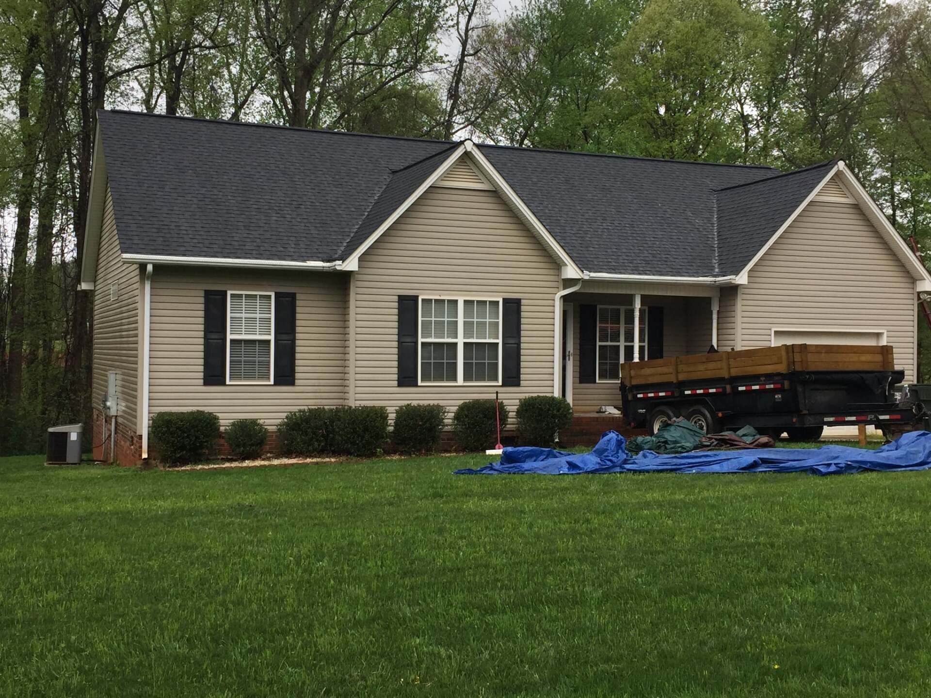 A house with a blue tarp on the grass in front of it.