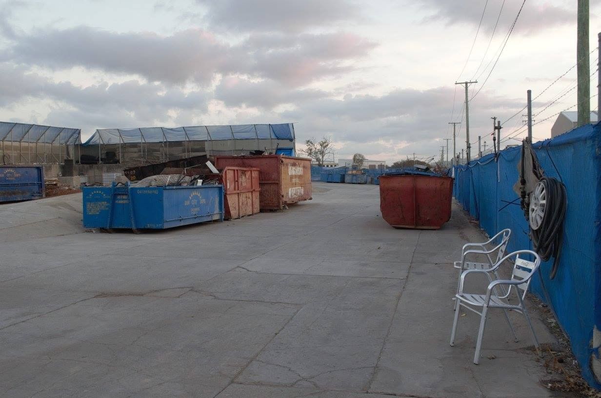 Rows Of Skip Bins are in Parking Lot Next To A Blue Fence — Sun City Skips In Bohle, QLD