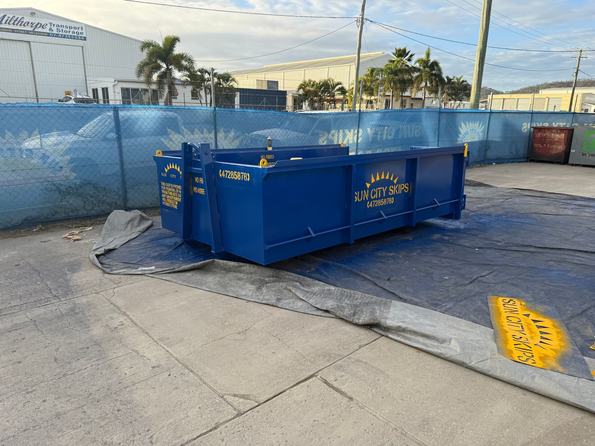 A Green Dumpster Filled With Wood Is In Front Of A Building Under Construction — Sun City Skips In Bohle, QLD