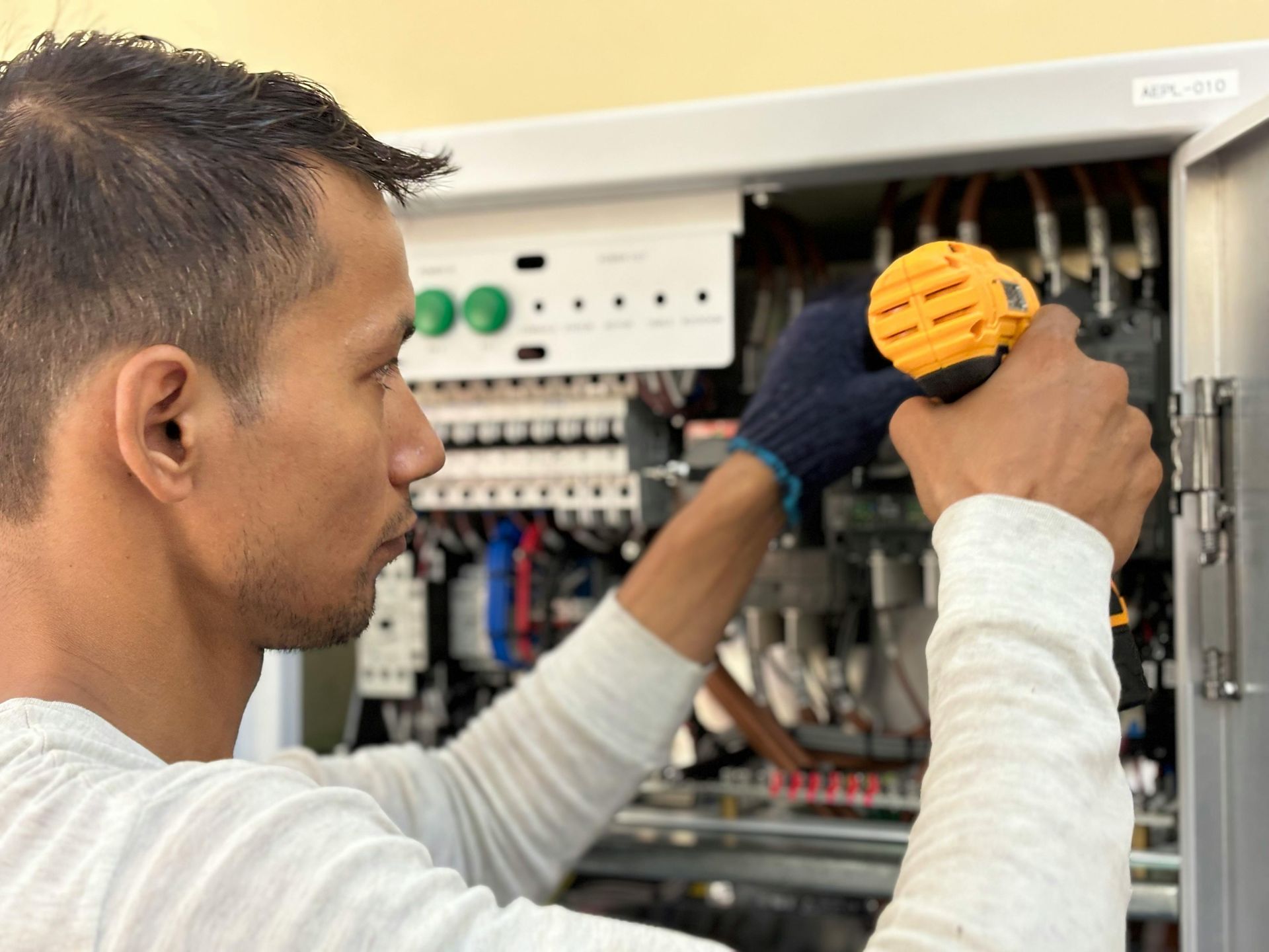 Two technicians in blue uniforms and hard hats inspect a machine control panel while referencing a laptop computer.