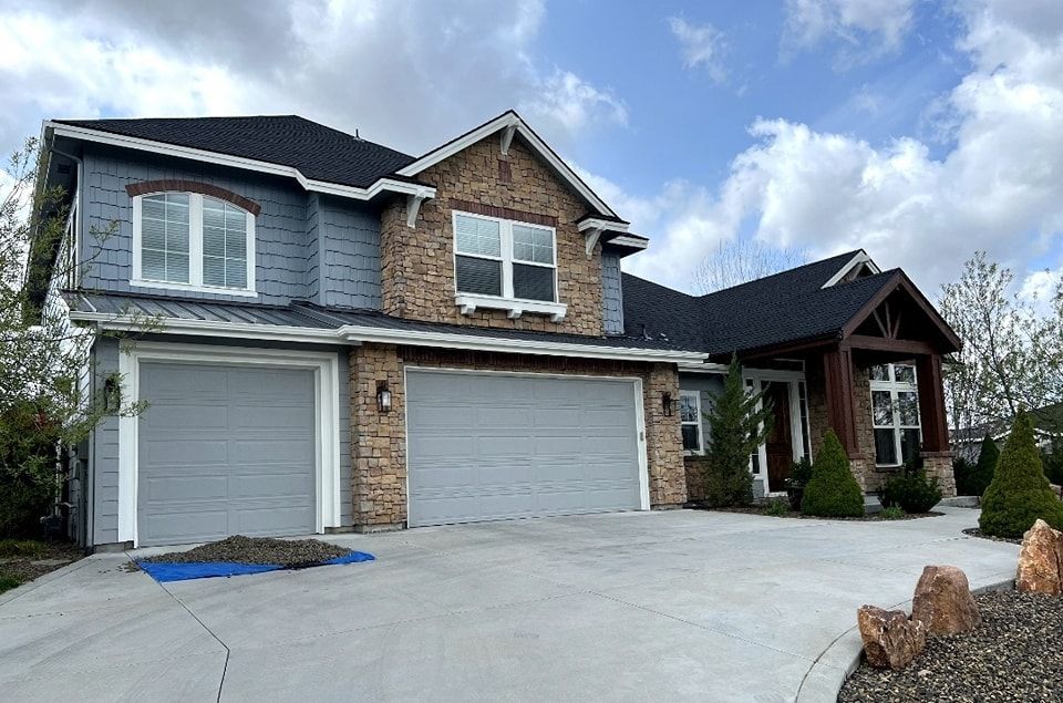 A large house with two garage doors and a blue tarp in front of it.