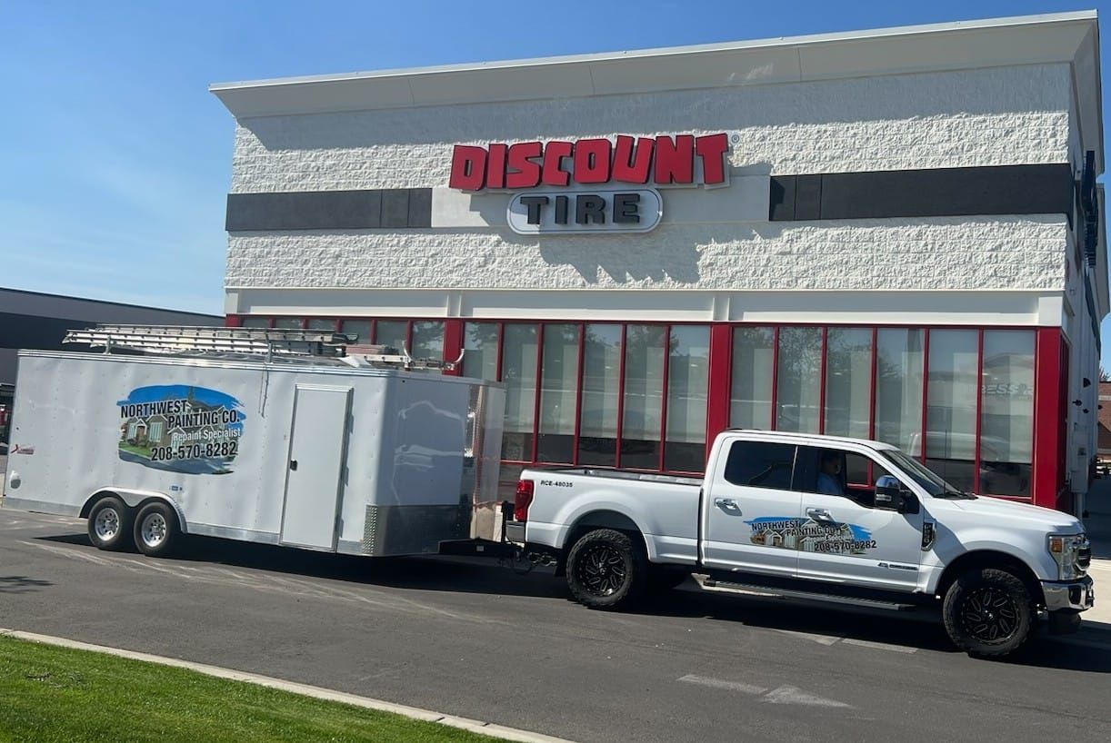 A white truck with a trailer attached to it is parked in front of a discount tire store.