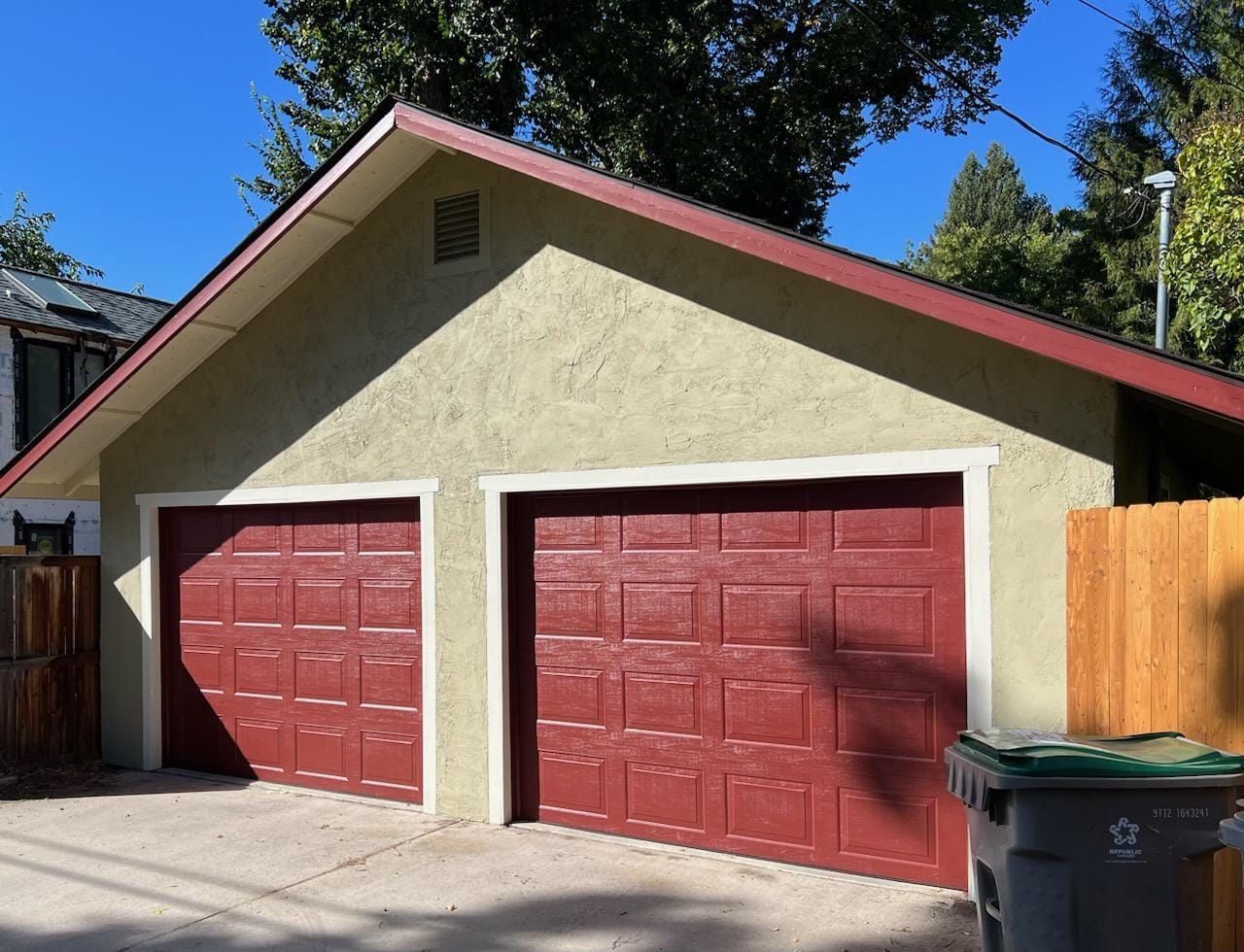 A garage with two red garage doors and a trash can in front of it
