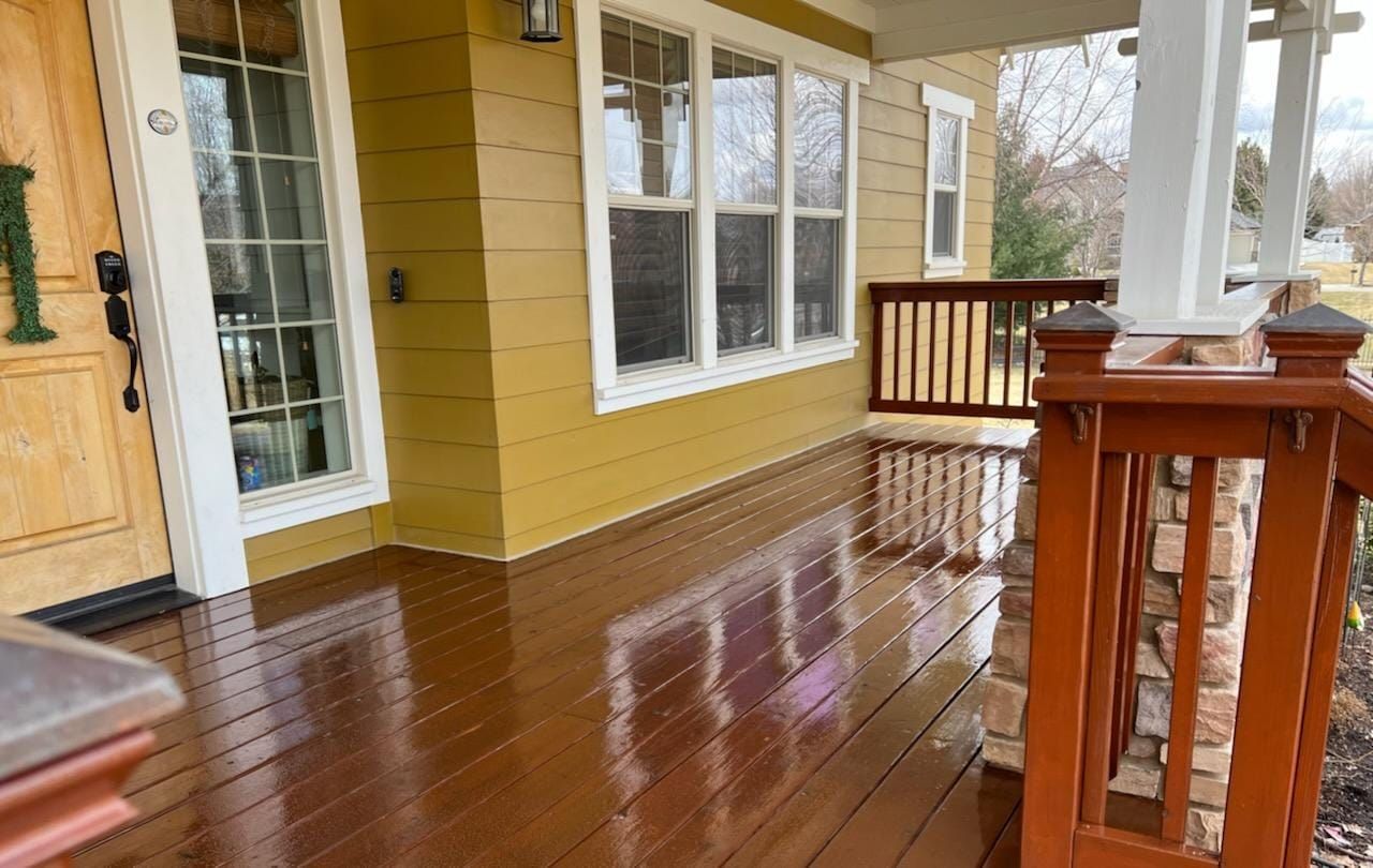 The front porch of a house with a wooden deck and a wooden railing.