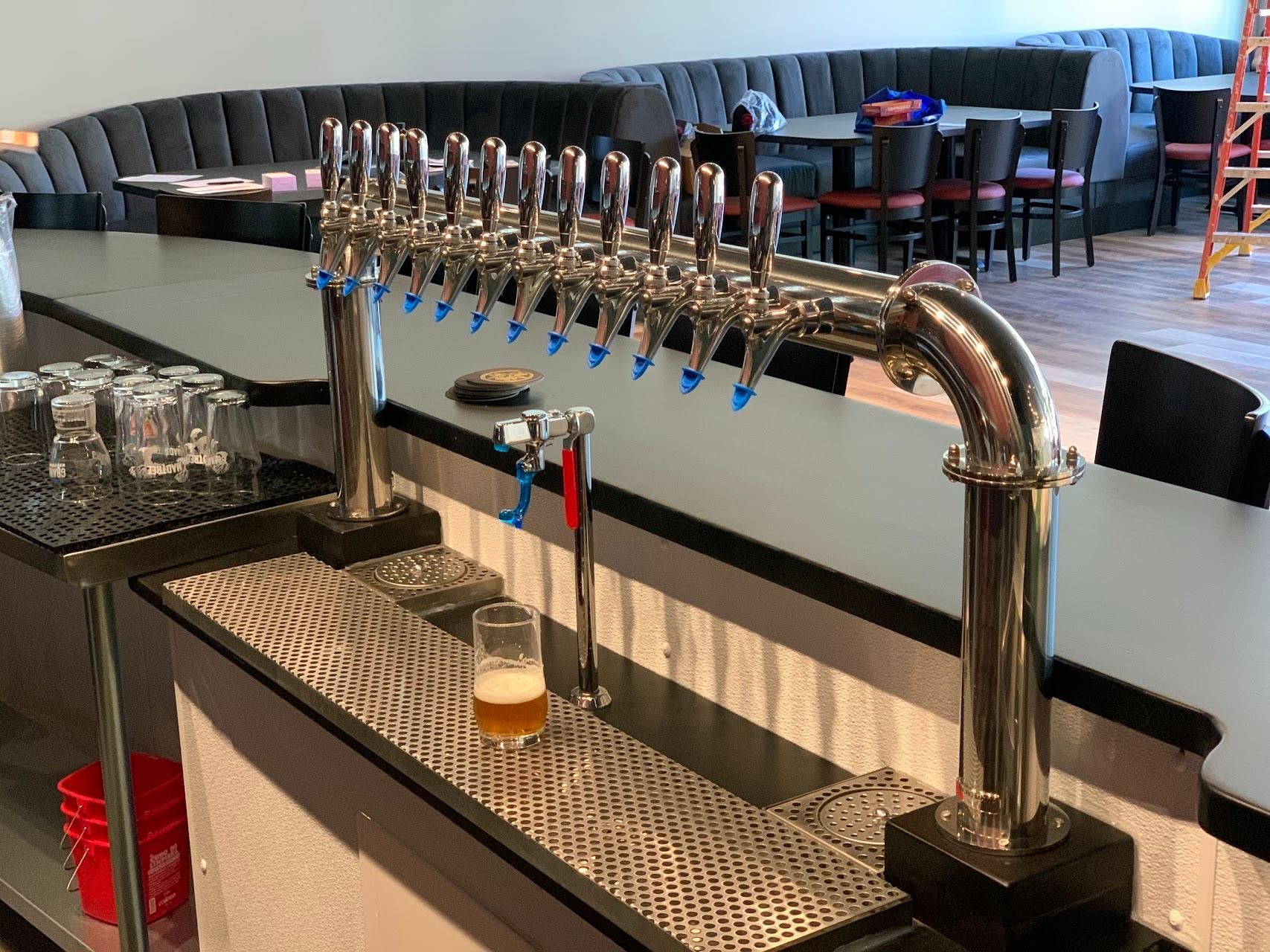 A bar with a lot of taps and a glass of beer on the counter.