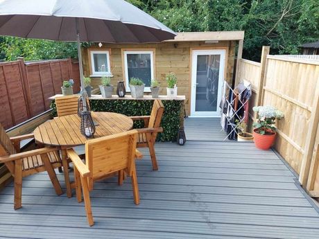 Garden building with a table, chairs, decking, fencing, and a summer house at the end of the garden.