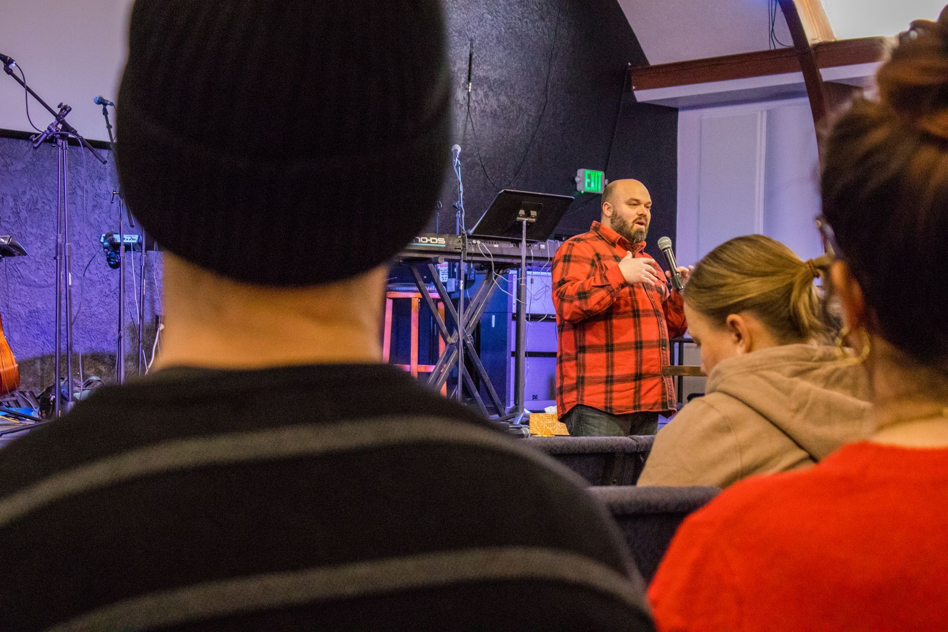 A man in a plaid shirt is giving a speech to a group of people.