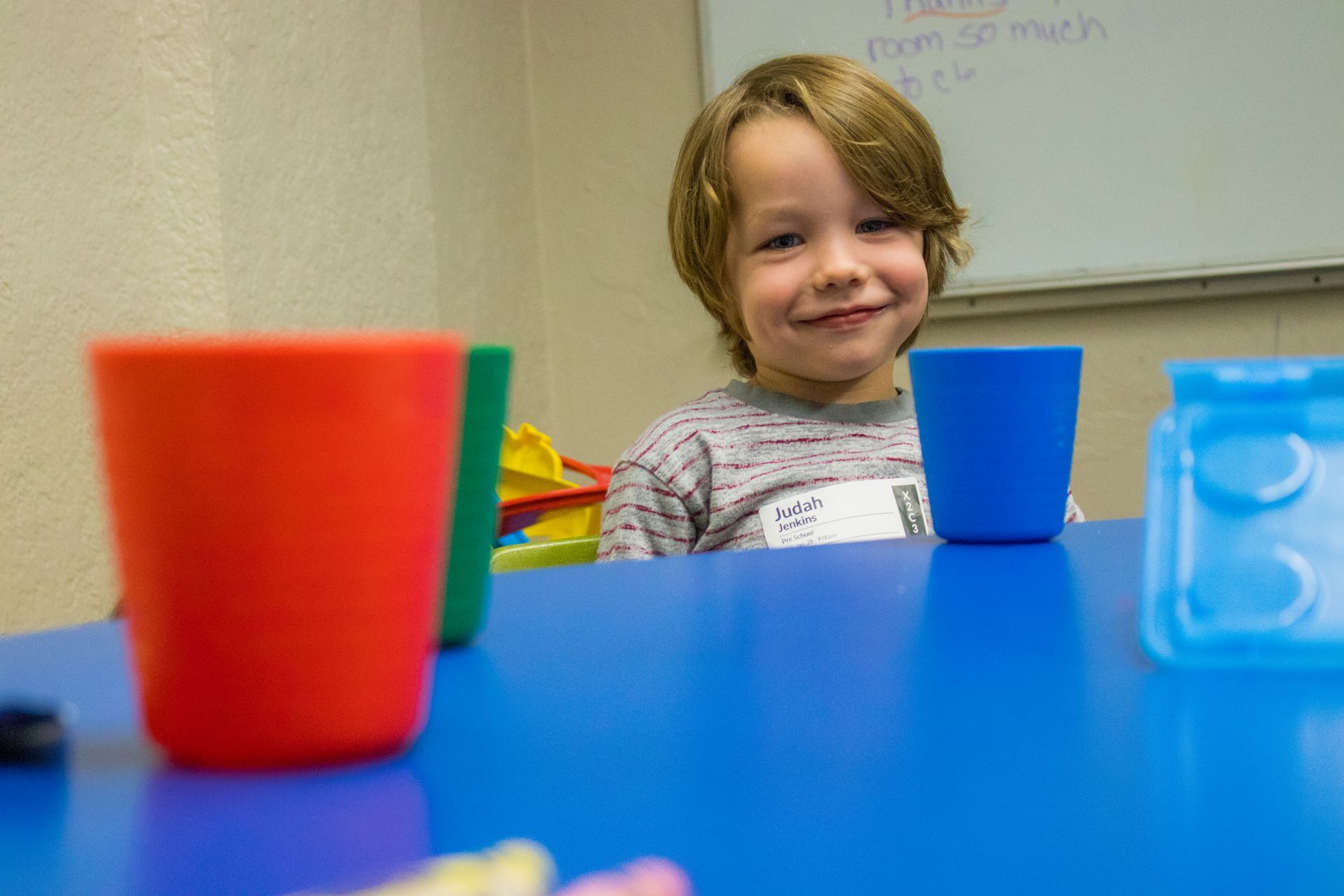 A young boy is sitting at a table with cups and toys.