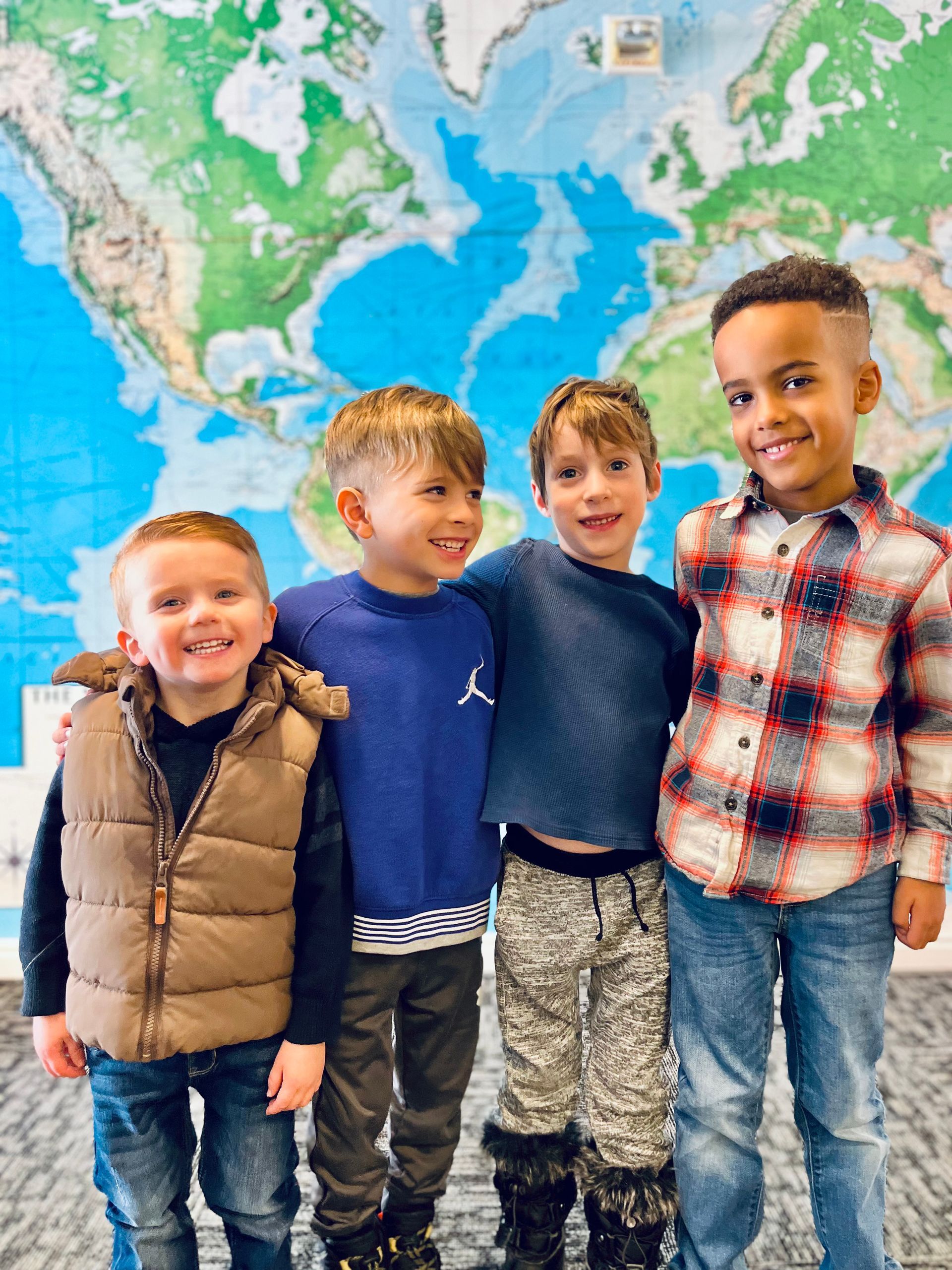 Four young boys are posing for a picture in front of a map of the world.