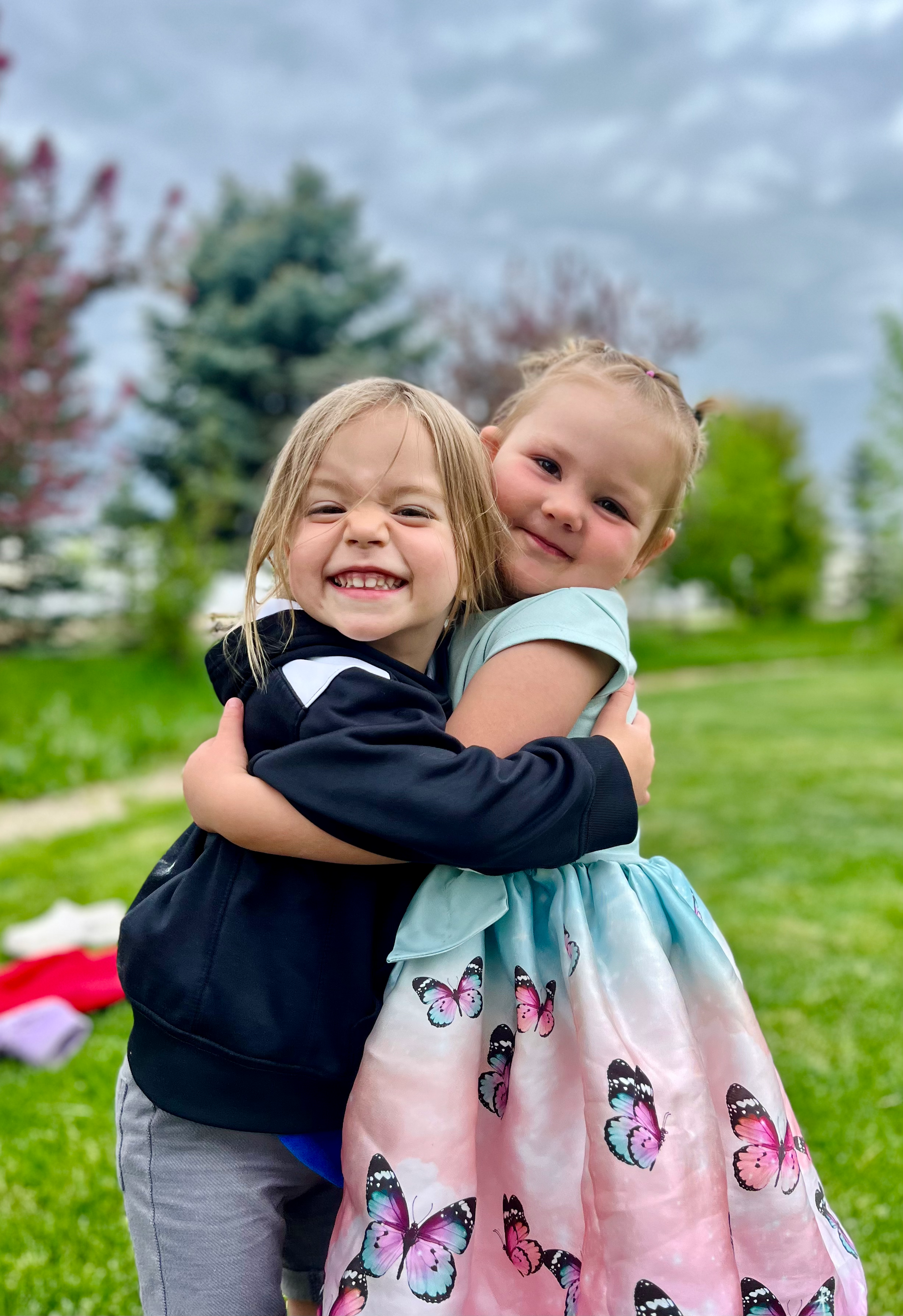 Two little girls are hugging each other in a park.
