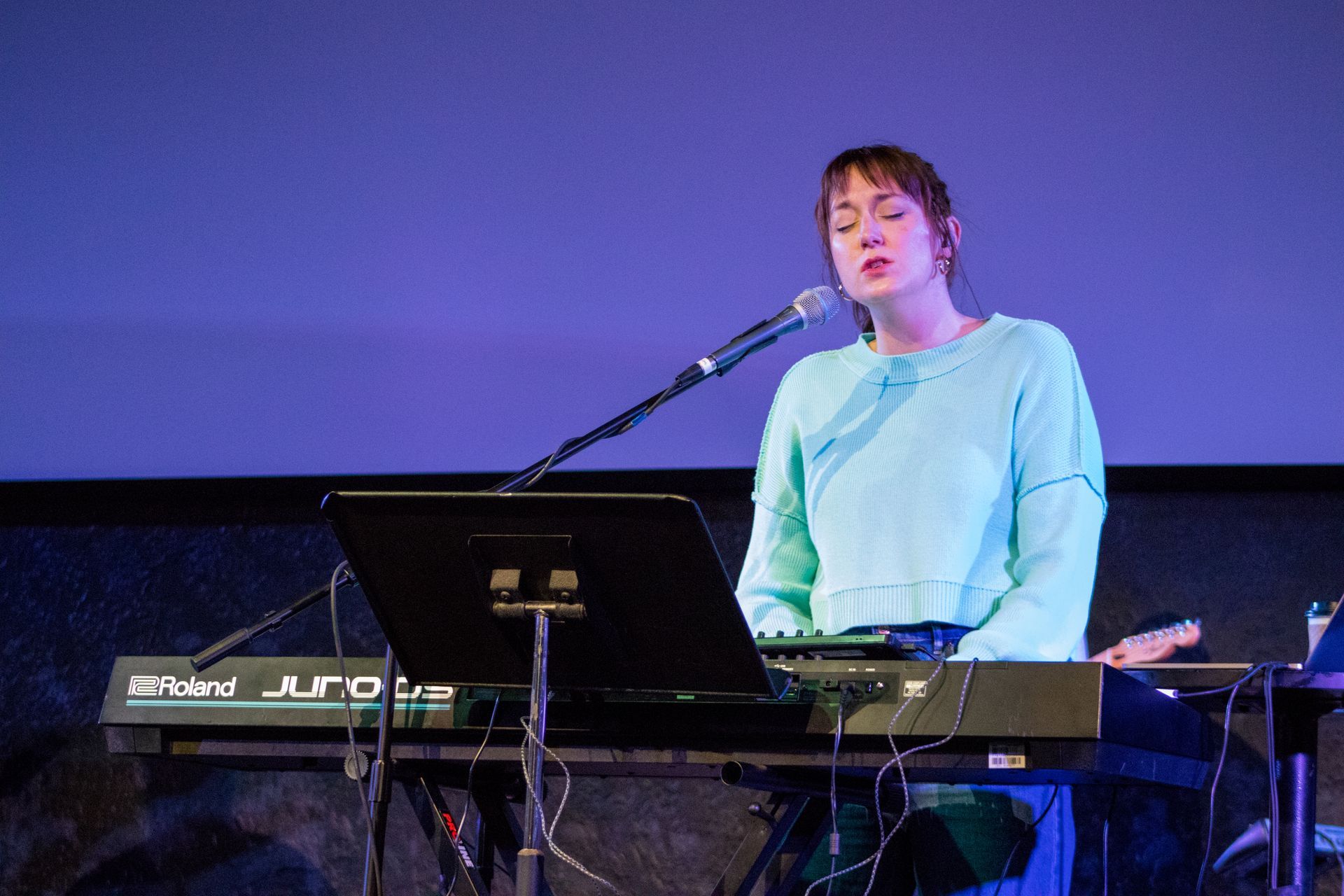 A woman is singing into a microphone while playing a keyboard.