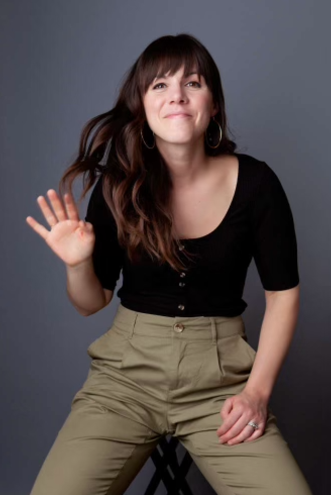 A woman in a black top and khaki pants is waving her hand
