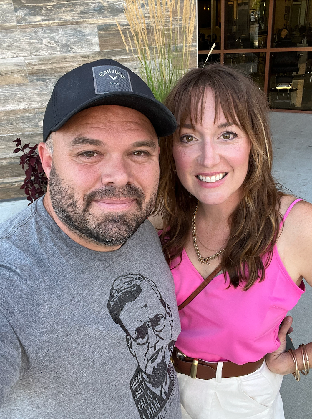 A man and a woman are posing for a picture together . the woman is wearing a pink tank top.