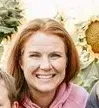 A woman is smiling while standing next to a child in front of a sunflower.