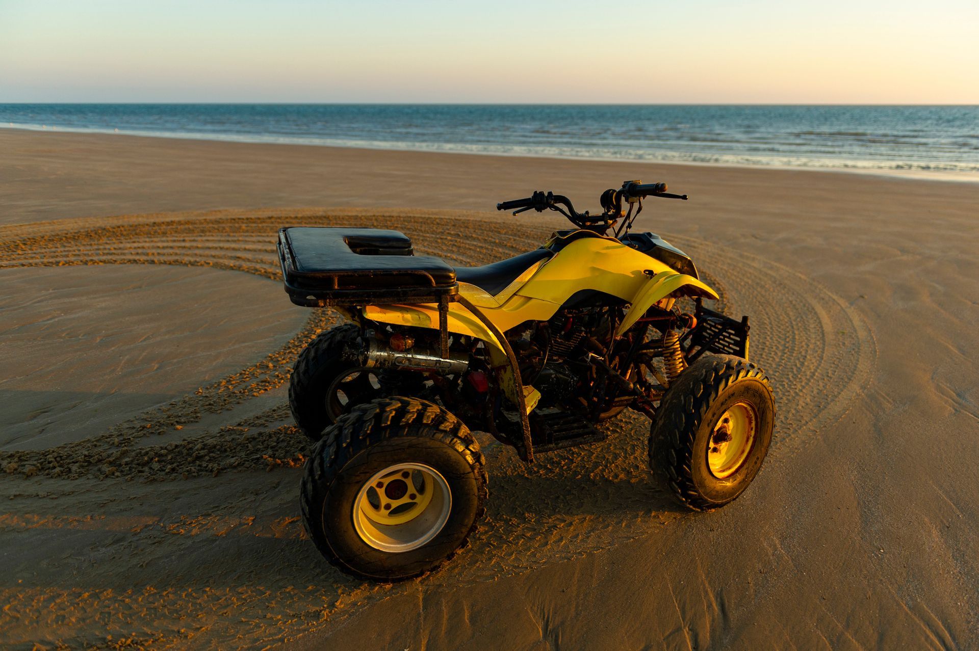Yellow ATV parked on a sandy beach with ocean in the background during a sunset.