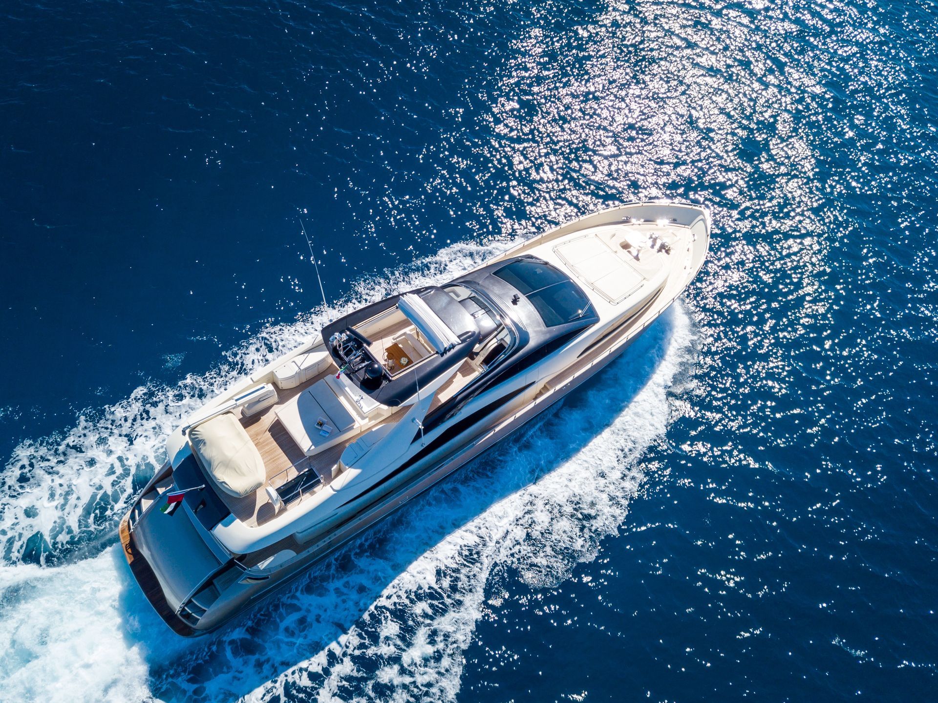 Aerial view of a white and gray yacht cruising on blue water, leaving a white wake.