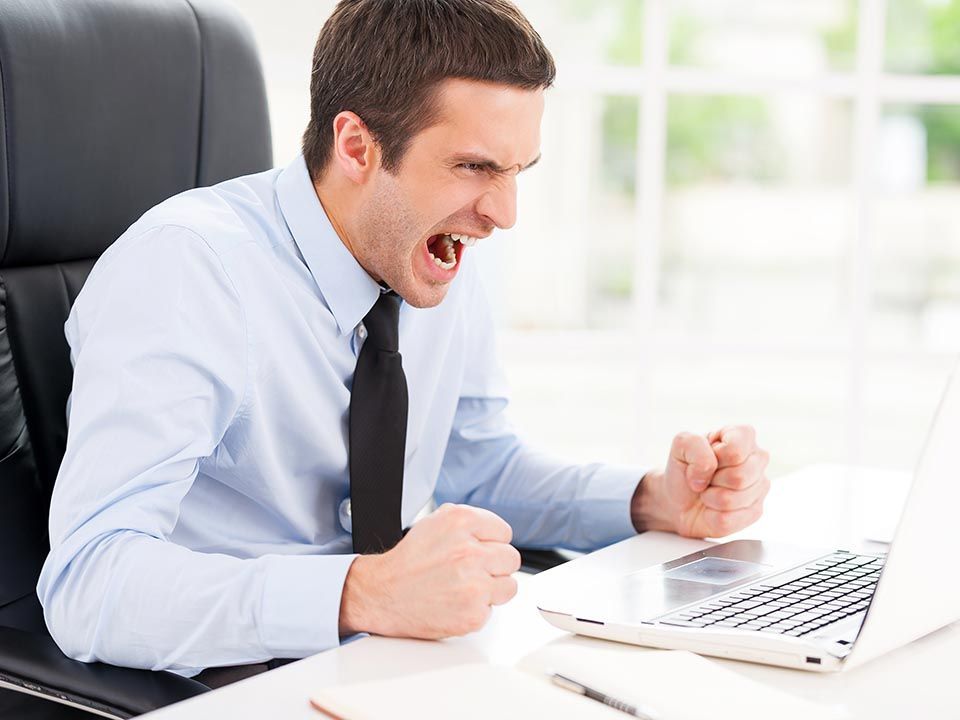 A man is sitting in front of a laptop computer with his fist in the air.
