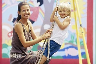 A woman is sitting next to a child on a swing.