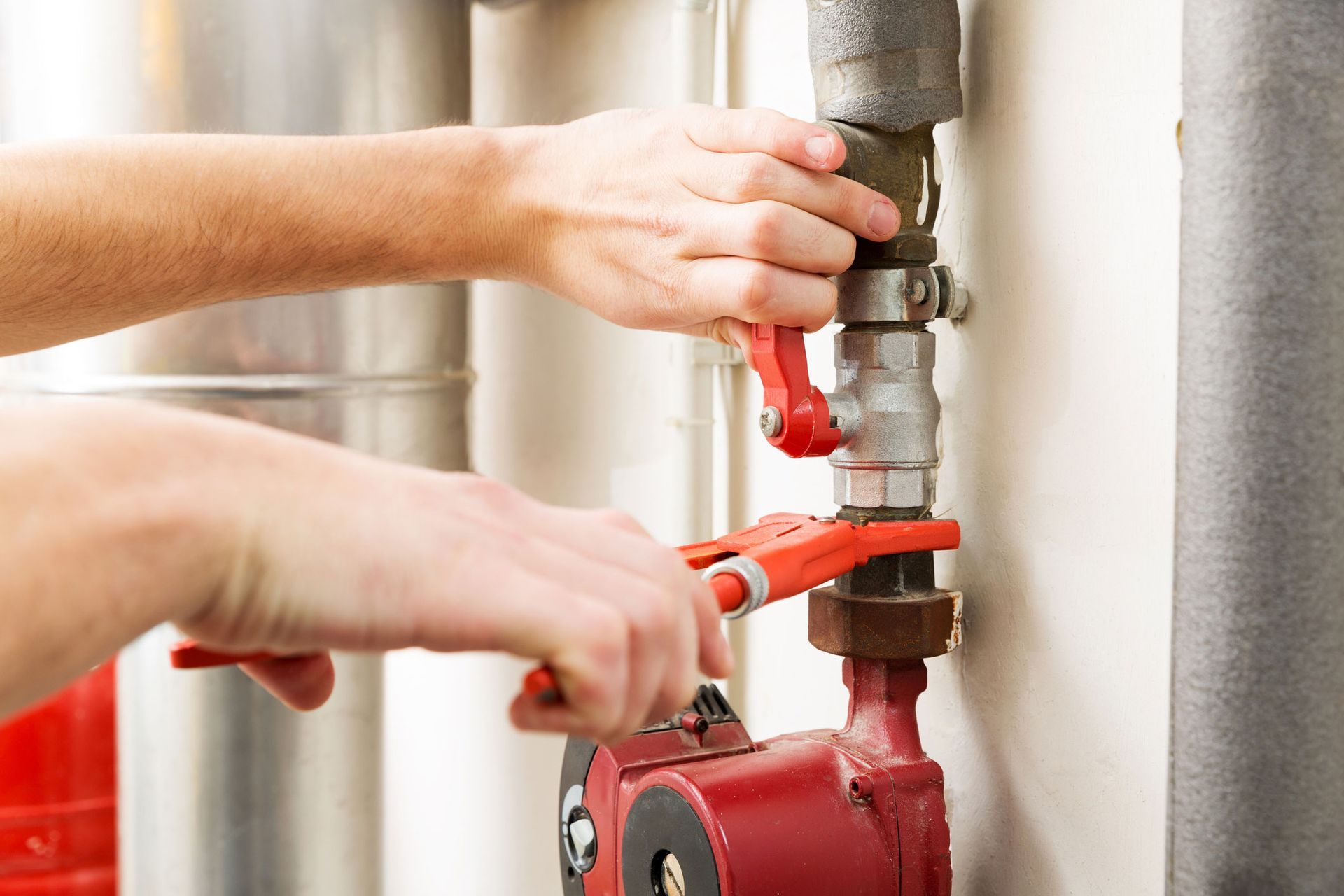 Person using a wrench to adjust a red valve on a heating system, indoors.