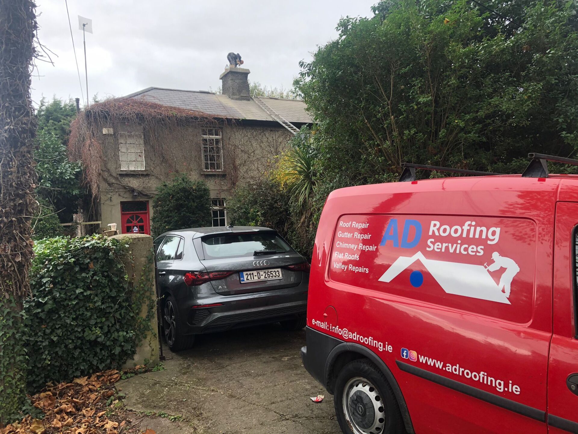 A red roofing services van is parked in front of a house.