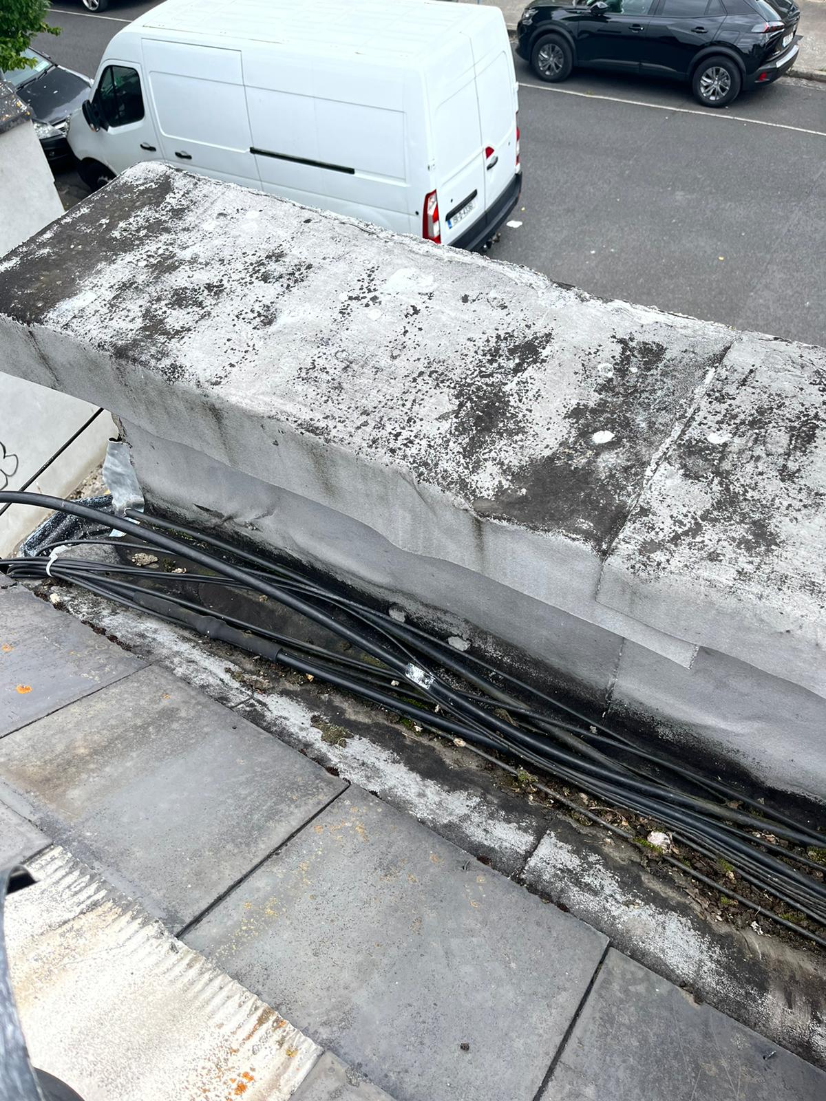 A white van is parked on the side of the road next to a concrete wall.