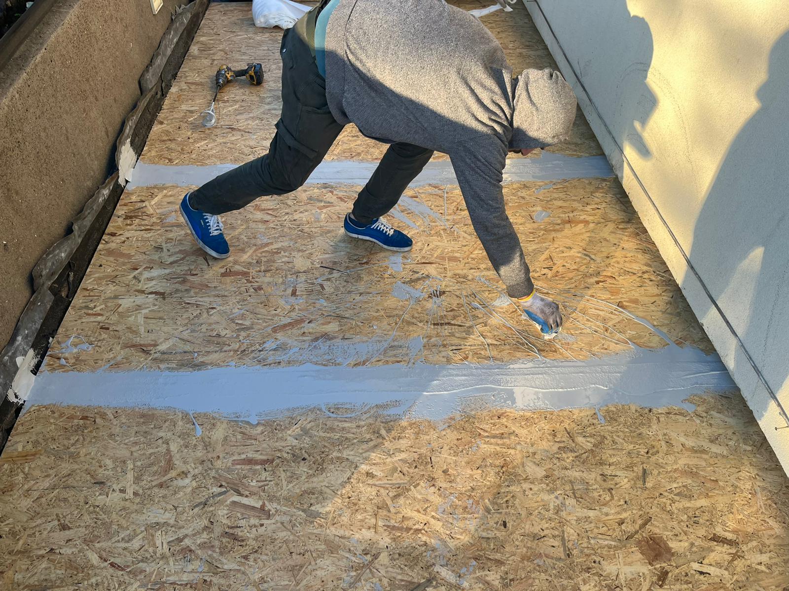 A man is painting a wooden floor with a brush.