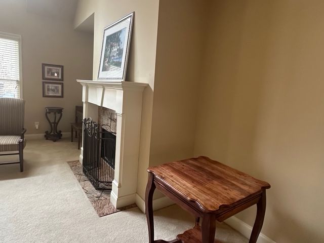 Living room with a fireplace, side table, beige walls, and carpet. Living room with a fireplace, side table, beige walls, and carpet.