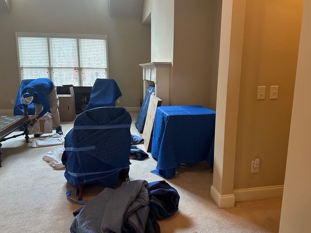Movers wrapping furniture in blue pads in a living room, preparing for a move. Movers wrapping furniture in blue pads in a living room, preparing for a move.