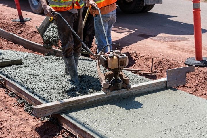 Concrete workers screeding and leveling a freshly poured concrete slab in formwork
