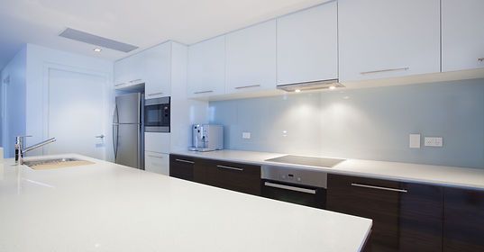 A modern kitchen featuring white upper cabinets, dark wood lower cabinets, white countertops, and stainless appliances.