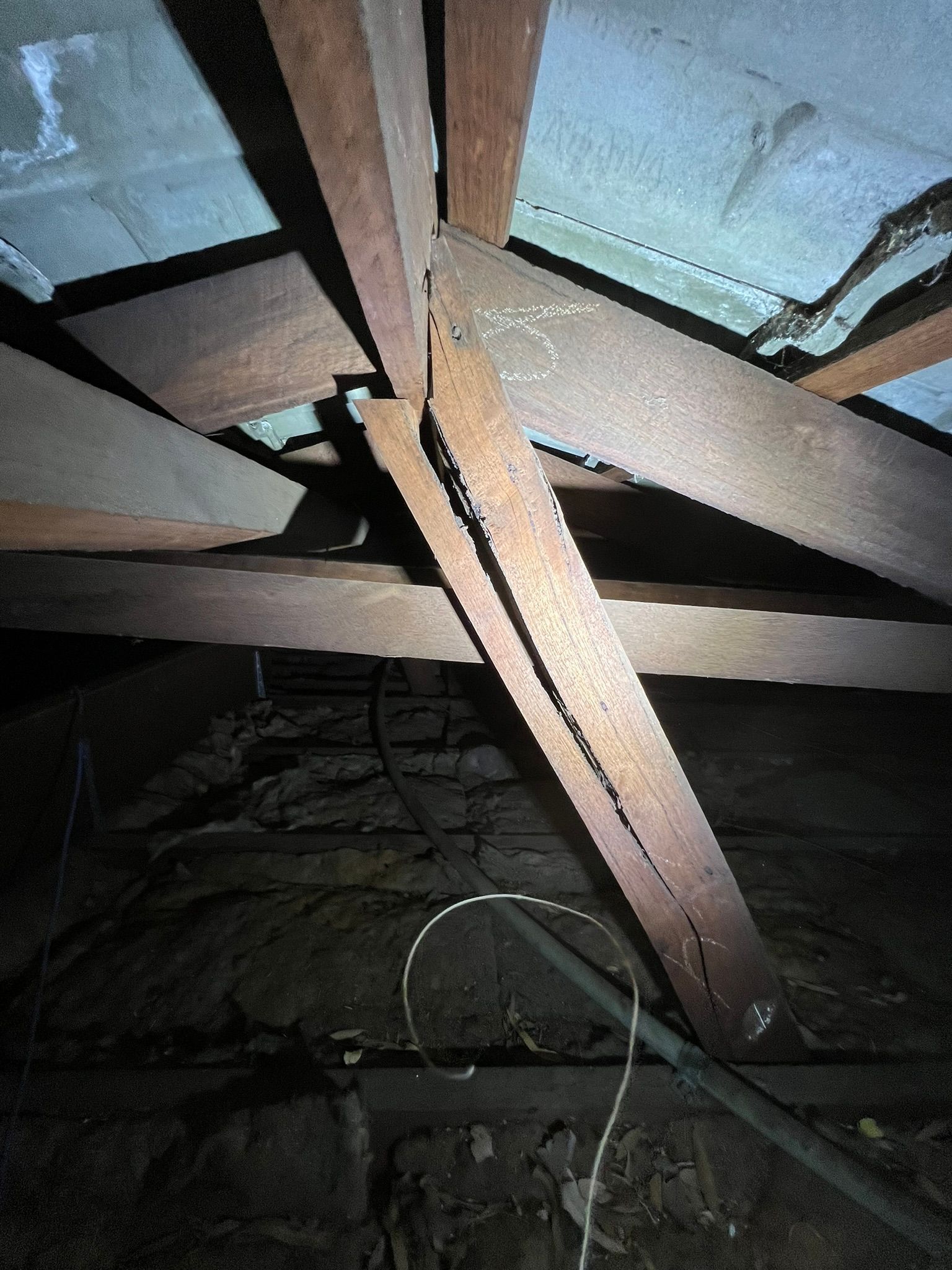 A structural view of an attic showing a cracked wooden rafter support beam, dimly lit against the roof and insulation.