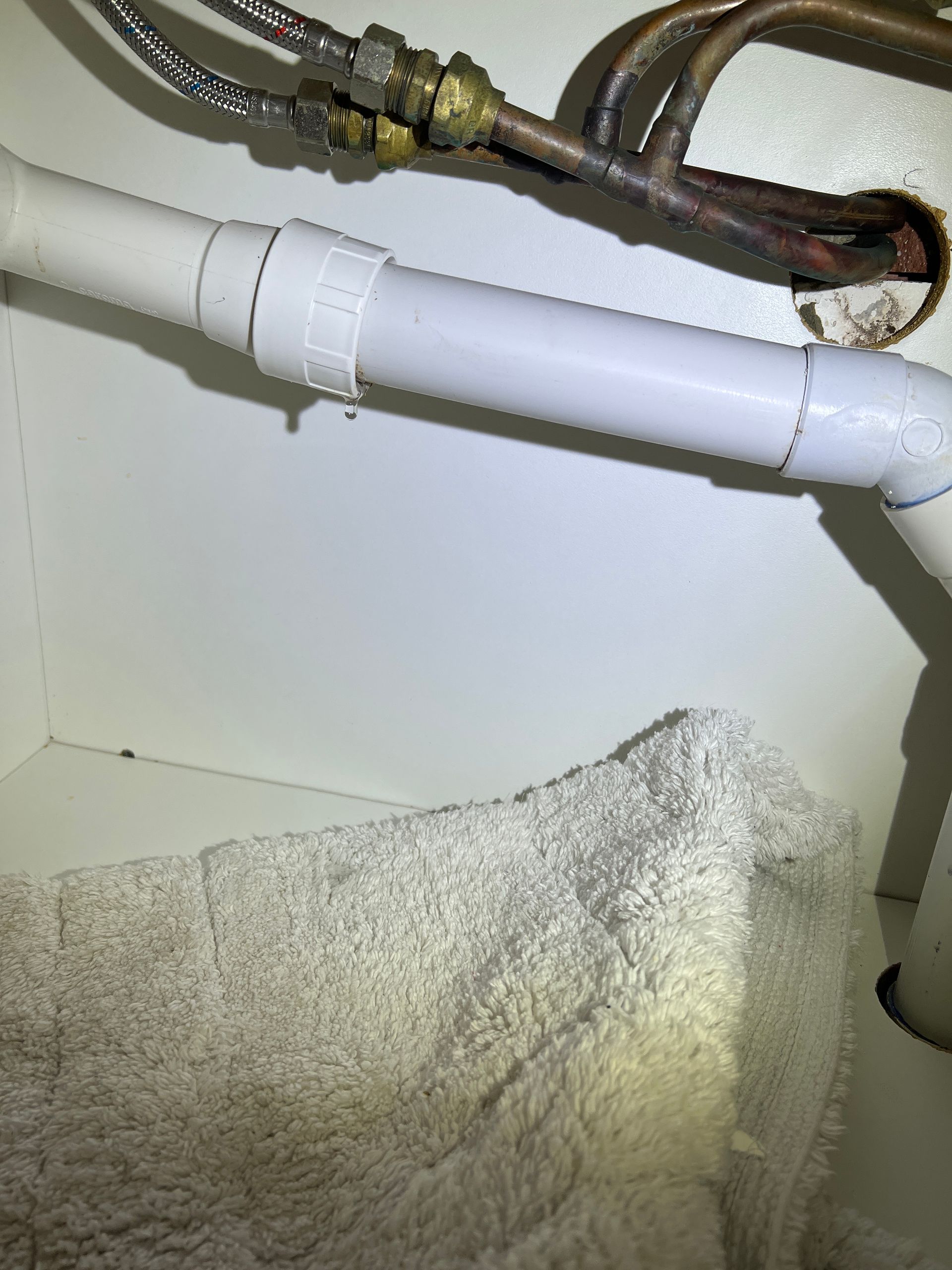 White plastic plumbing pipes under a sink with a towel placed beneath a leaking joint.